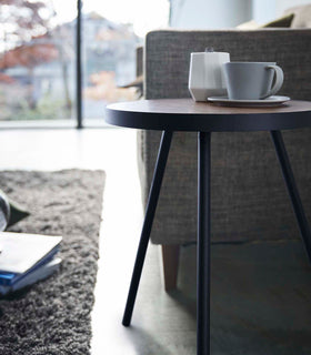 Close-up profile view of Black Side Table by Yamazaki Home next to a sofa, holding a cup and a saucer. view 11