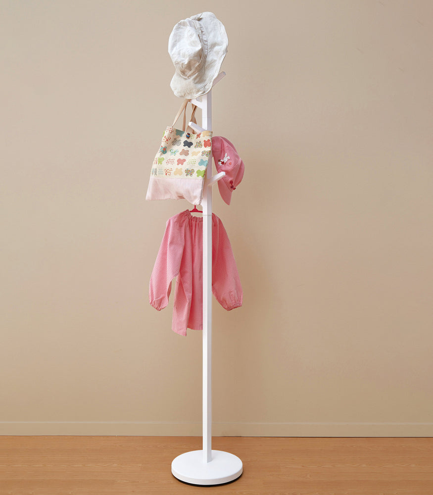 View 4 - White coat rack in the shape of a tree hung with children's clothes and hats.