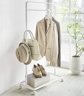 White Rolling Coat Rack holding clothes and fashion accessories by Yamazaki Home. view 4