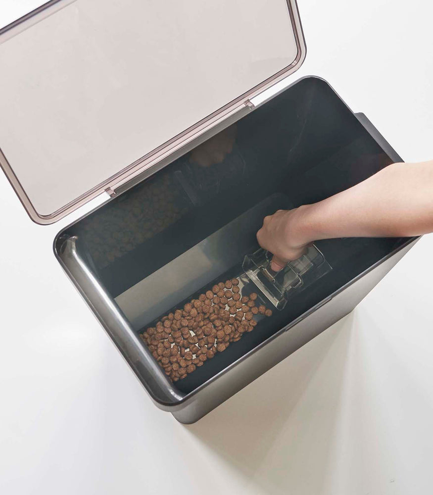 View 39 - Aerial view of person scooping pet food out of black Airtight Food Storage Container on white background by Yamazaki Home.
