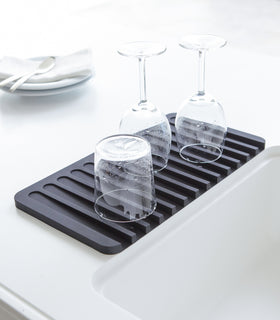 Black Dish Drainer Tray containing dinnerware on sink counter by Yamazaki Home. view 4