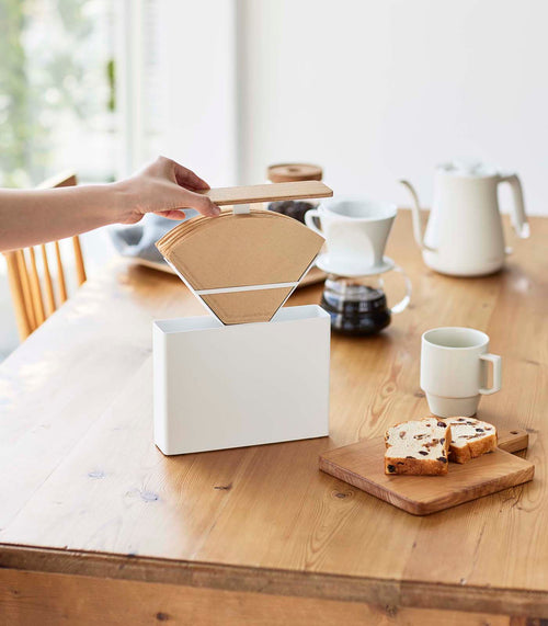 Front view of person lifting Coffee Filter Case's cover to reveal coffee filters on table by Yamazaki Home.