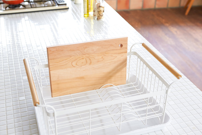 White Dish Rack next to kitchen sink holding a cutting board by Yamazaki Home.