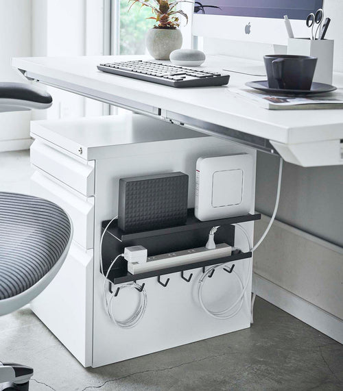 Black Wall-Mount Cable and Router Storage Rack attached to side of cabinet holding router and power cord by Yamazaki Home.
