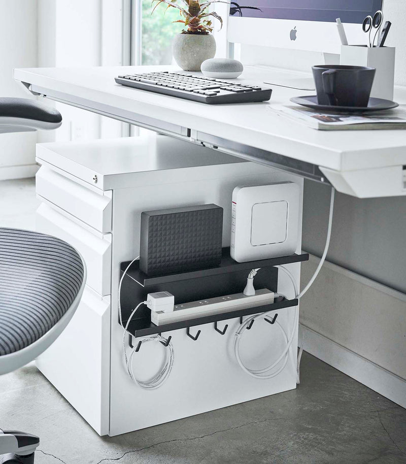 Black Wall-Mount Cable and Router Storage Rack attached to side of cabinet holding router and power cord by Yamazaki Home.