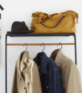 Close up front view of black Leaning Coat Rack with Shelf holding bag, hat, and coats by Yamazaki Home. view 5
