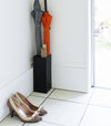 Compact Black Umbrella Stand in entryway holding two umbrellas, and one foldable umbrella by Yamazaki home.