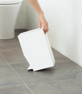 Side view of white Step Trash Can held by handle in bathroom by Yamazaki Home. view 5