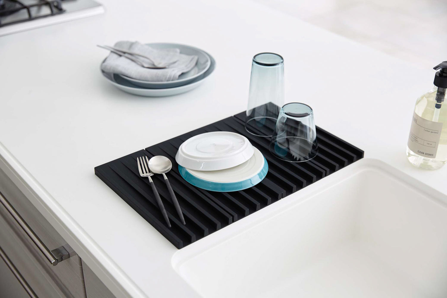 View 8 - Black Folding Dish Drainer Mat holding plates, cups, and silverware on kitchen counter by Yamazaki Home.