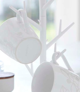 Close up view of white Glass & Mug Tree displaying mugs by Yamazaki Home. view 4
