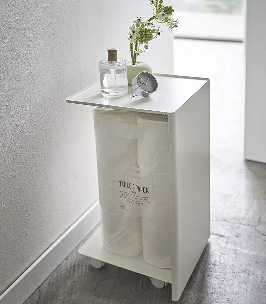 View 5 - Side view of white Rolling Bathroom Organizer holding toilet paper and displaying décor pieces in bathroom by Yamazaki Home.