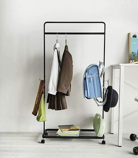 Front view of black Rolling Coat Rack holding school clothes and supplies by Yamazaki Home. view 9