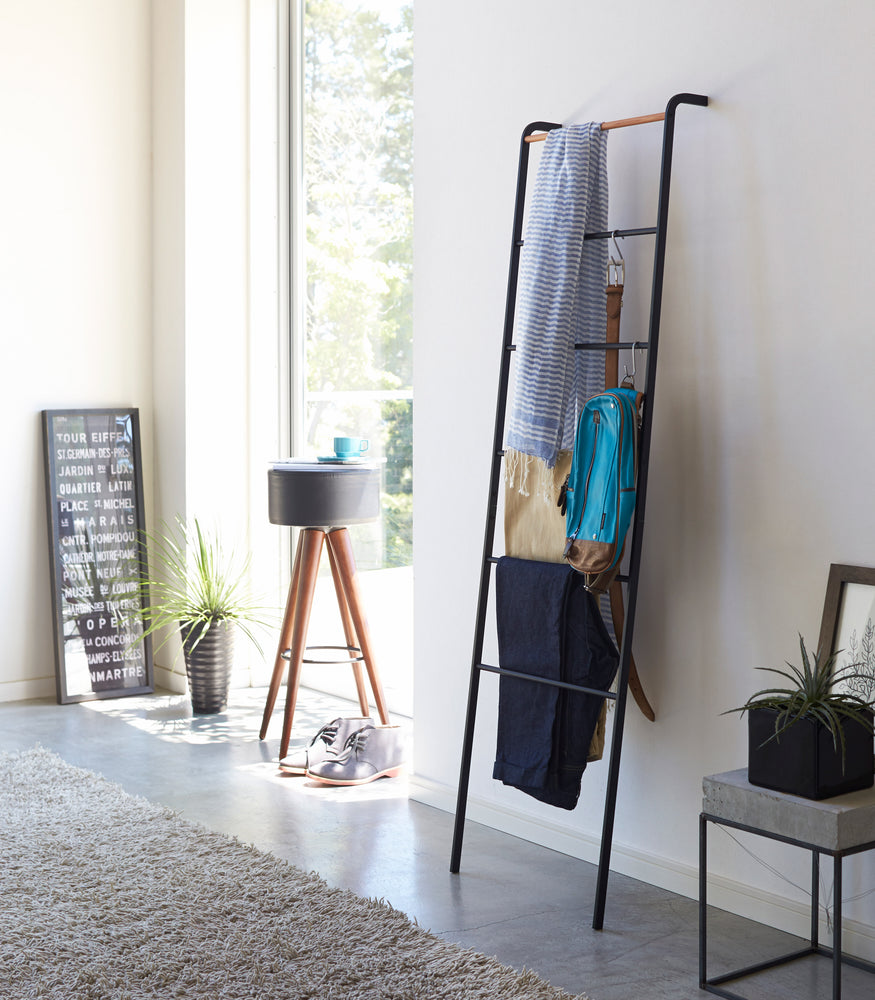 View 6 - Black Leaning Ladder Rack holding clothing items and accessories in bedroom by Yamazaki Home.