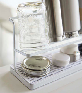 Close up view of white Countertop Bottle Drying Rack holding mason jar, bottles, and covers by Yamazaki Home. view 5
