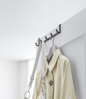 Black Over-the-Door Hanger holding purse and jacket on closet door by Yamazaki Home. view 10