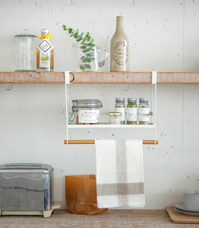 Front view of white Undershelf Organizer holding spices and towel by Yamazaki Home. view 2