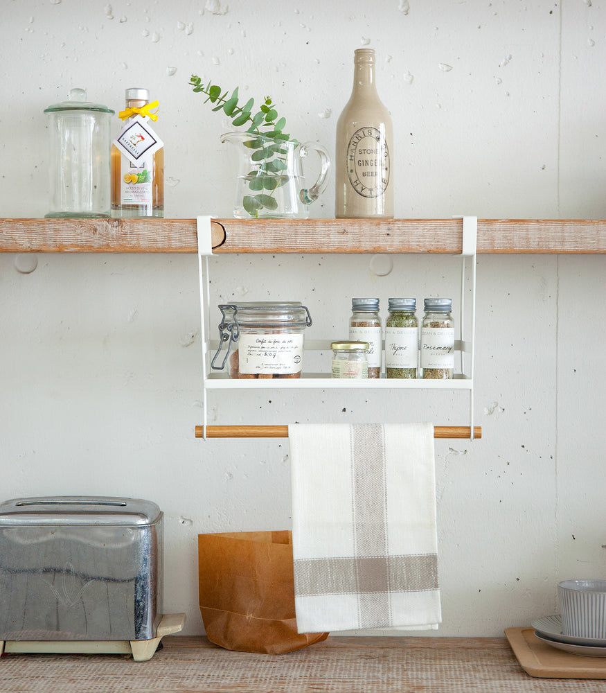View 2 - Front view of white Undershelf Organizer holding spices and towel by Yamazaki Home.