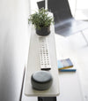 Side view of white Compliant TV Shelf holding smart home device, plant, and remote by Yamazaki Home.