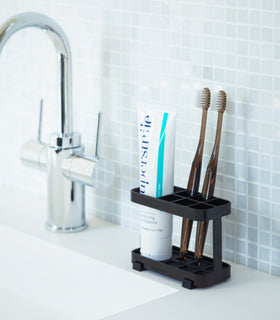 Black Toothbrush Stand holding toothbrushes and toothpaste on bathroom sink counter by Yamazaki Home. view 6
