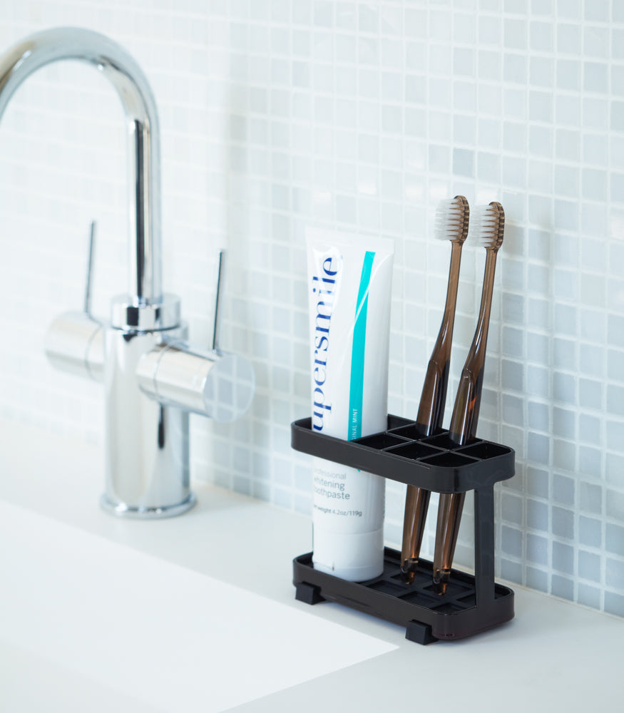 View 6 - Black Toothbrush Stand holding toothbrushes and toothpaste on bathroom sink counter by Yamazaki Home.