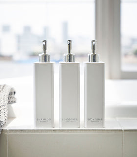 Front view of Yamazaki Home white Shampoo, Conditioner, and Body Soap dispensers in bathroom. view 3