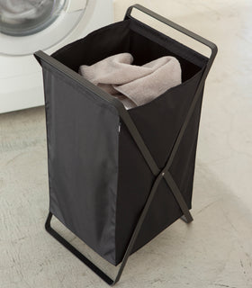 Black Laundry Hamper Storage Organizer holding towel in laundry room by Yamazaki Home. view 10
