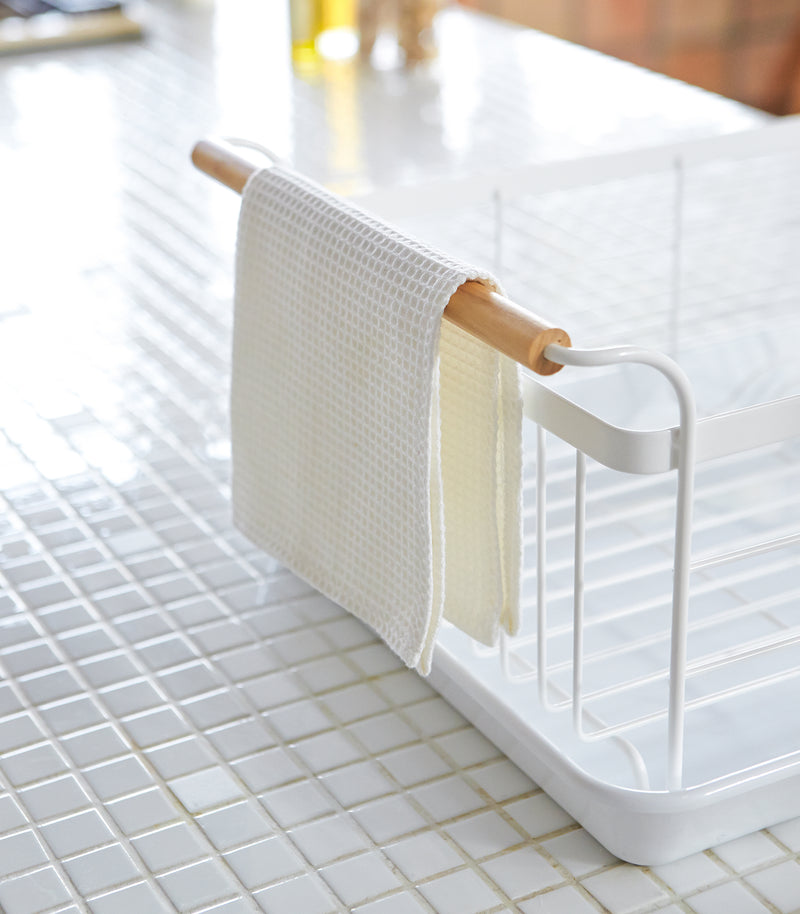 Side view of wooden handle on white Dish Rack  holding  washcloth by Yamazaki Home.