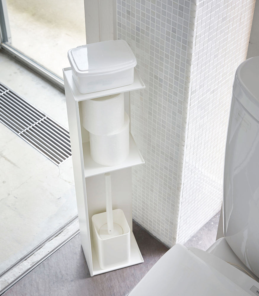 View 3 - Yamazaki Home white Toilet Organizer holding wet wipe case, toilet paper, and toilet brush in bathroom.