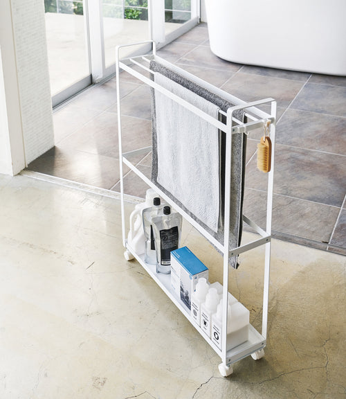 White Rolling Towel Rack holding cleaning products and towels by Yamazaki Home.