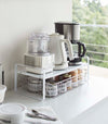 White Expandable Countertop Organizer expanded holding small appliances on kitchen countertop by Yamazaki Home.