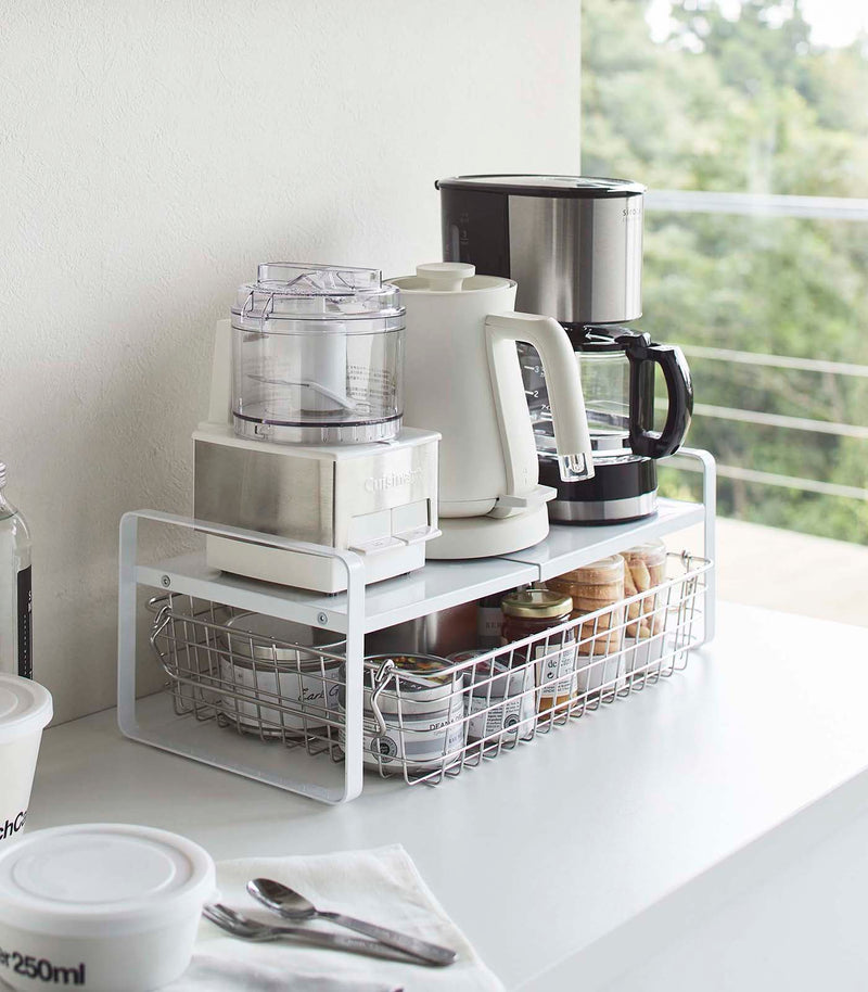 White Expandable Countertop Organizer expanded holding small appliances on kitchen countertop by Yamazaki Home.