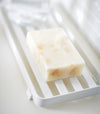 Close up side view of white Slotted Tray holding soap bar by Yamazaki Home.
