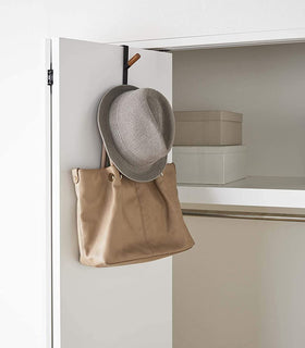 Black Over-the-Door Hook on closet door holding hat and bag by Yamazaki Home. view 11