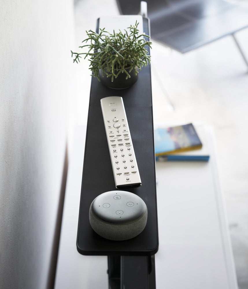 View 10 - Side view of black Compliant TV Shelf displaying remote, plant and smarthome device by Yamazaki Home.