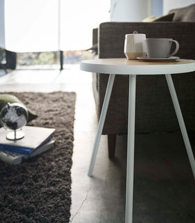 Close-up profile view of White Side Table by Yamazaki Home next to a sofa, holding a cup and a saucer. view 5