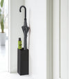 Compact Black Umbrella Stand in entryway holding one umbrella, and one foldable umbrella by Yamazaki home.
