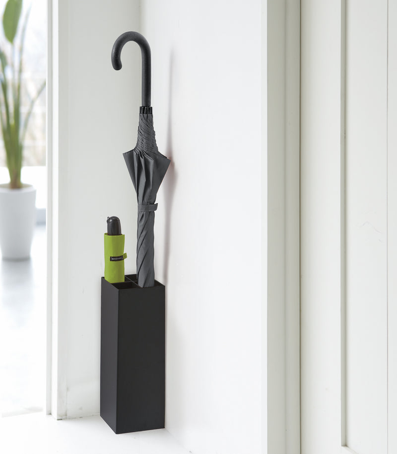 Compact Black Umbrella Stand in entryway holding one umbrella, and one foldable umbrella by Yamazaki home.