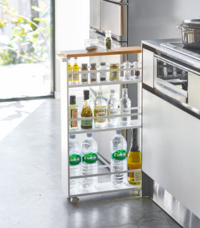 Front view of white Rolling Storage Cart holding spices and liquid items in kitchen by Yamazaki Home. view 2