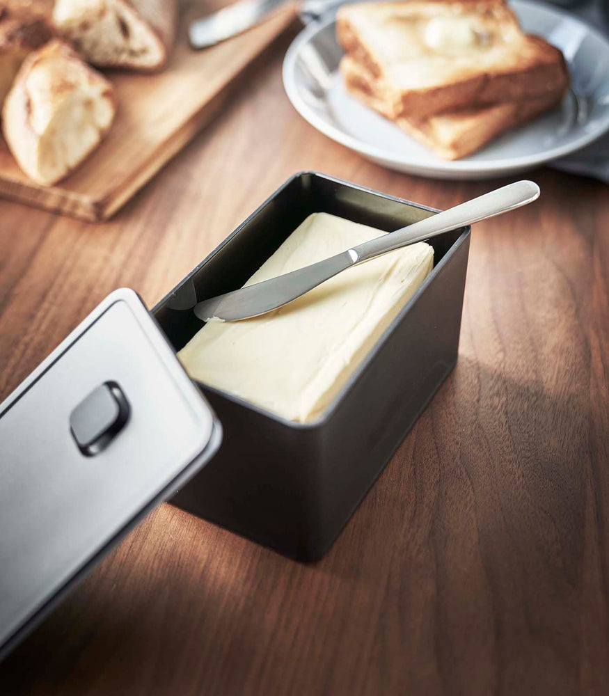 View 10 - Black Vacuum-Sealing Butter Dish holding butter on table by Yamazaki Home.