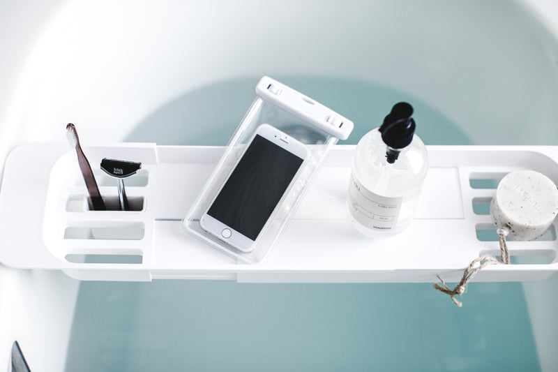 Aerial view of white Expandable Bathtub Caddy holding phone and beauty products by Yamazaki Home.