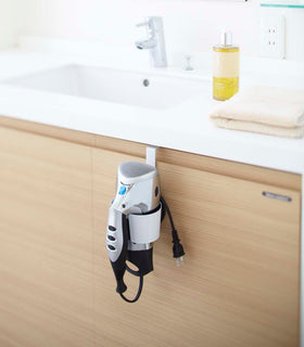 White Blow Dryer Holder holding blow dryer on bathroom cabinet by Yamazaki Home. view 2