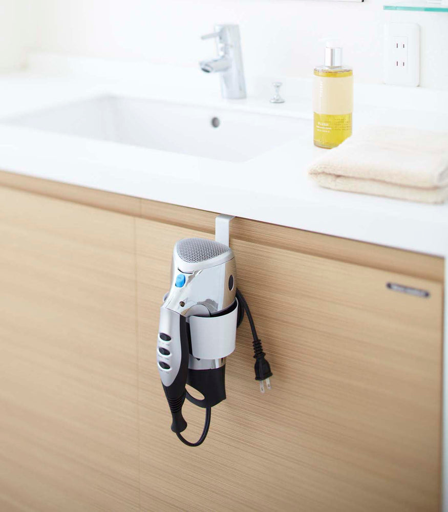 View 2 - White Blow Dryer Holder holding blow dryer on bathroom cabinet by Yamazaki Home.