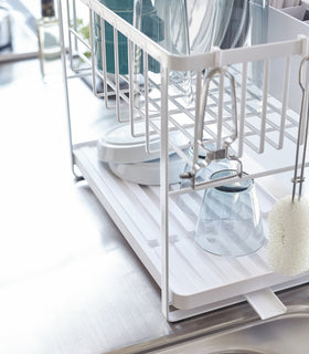 Side view of white Two-Tier Dish Rack holding dishware on upper rack and plates and cups on bottom rack by Yamazaki Home. view 5