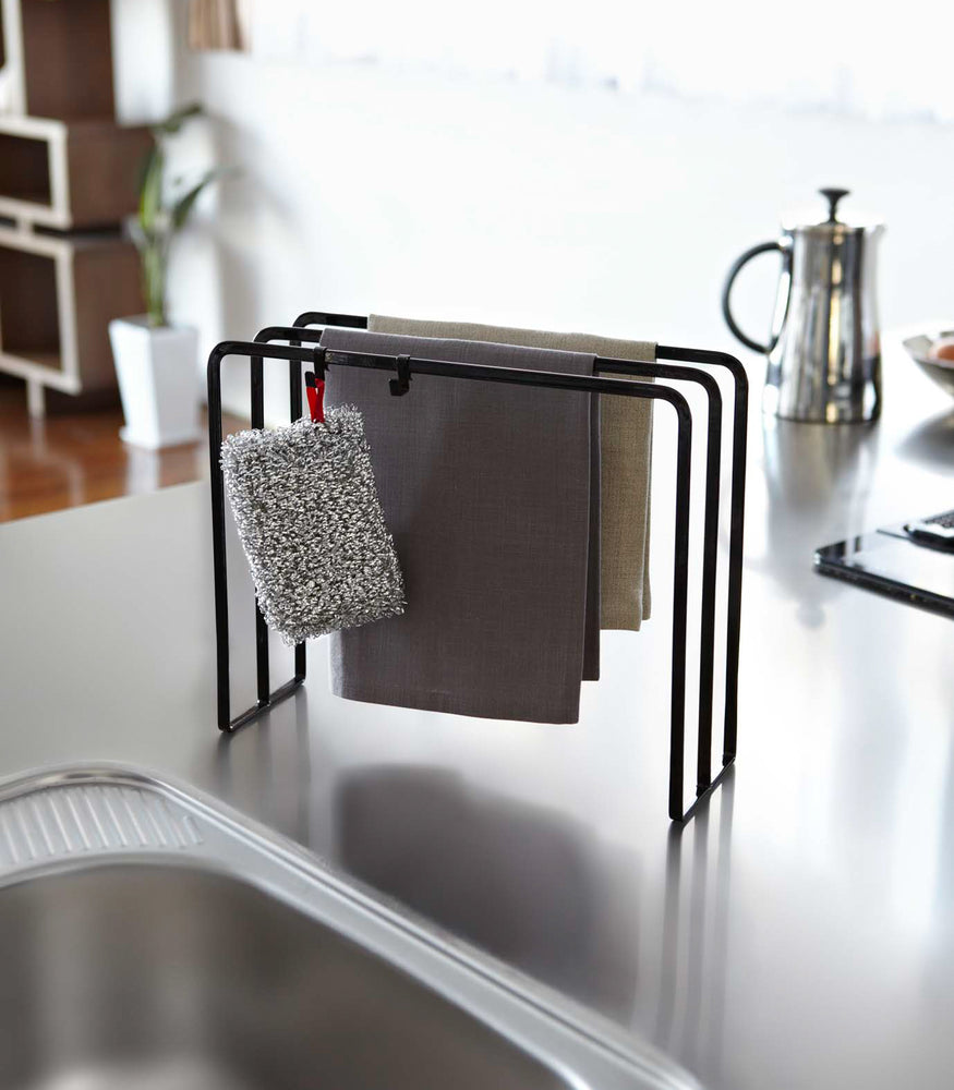 View 7 - Black Dish Towel Holder displaying towel and sponge on kitchen counter by Yamazaki Home.