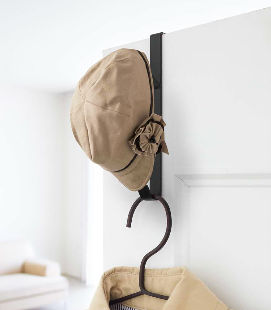 View 6 - Black Over-the-Door Hanger displaying hat and jacket on closet door by Yamazaki Home.