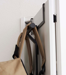Close up top view of Black Kids' Backpack Hanger holding a backpack on door by Yamazaki Home. view 10