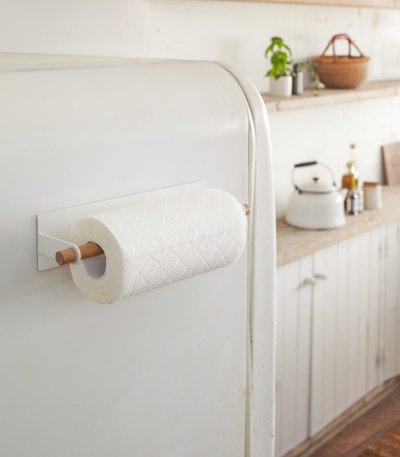 Wide view of Yamazaki's paper towel holder with wooden rod stuck to side of refrigerator, holding paper towels.
